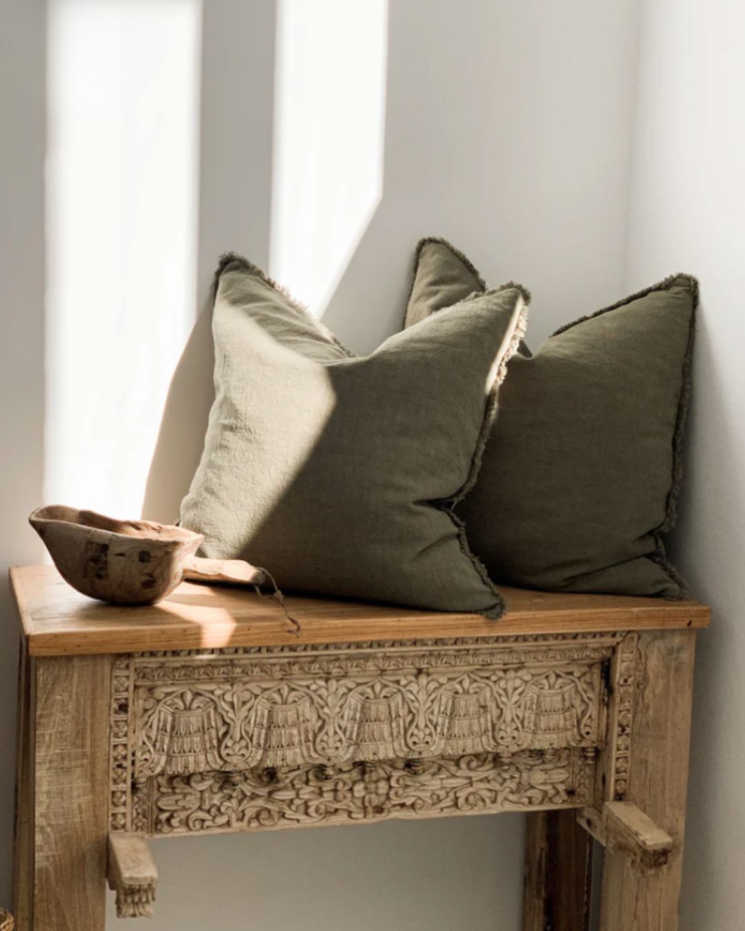 Olive green ramie cushion cover with hand-finished fringe edges on modern neutral sofa