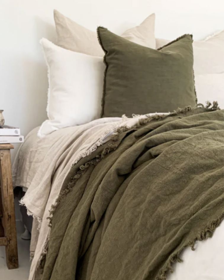 Green textured blanket and pillow on a bed with a wooden nightstand.