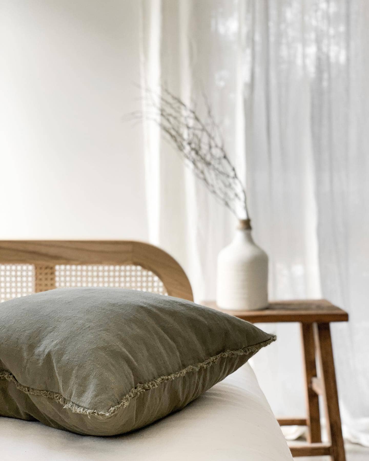 Green pillow on a bed with a wooden side table and white curtains in the background