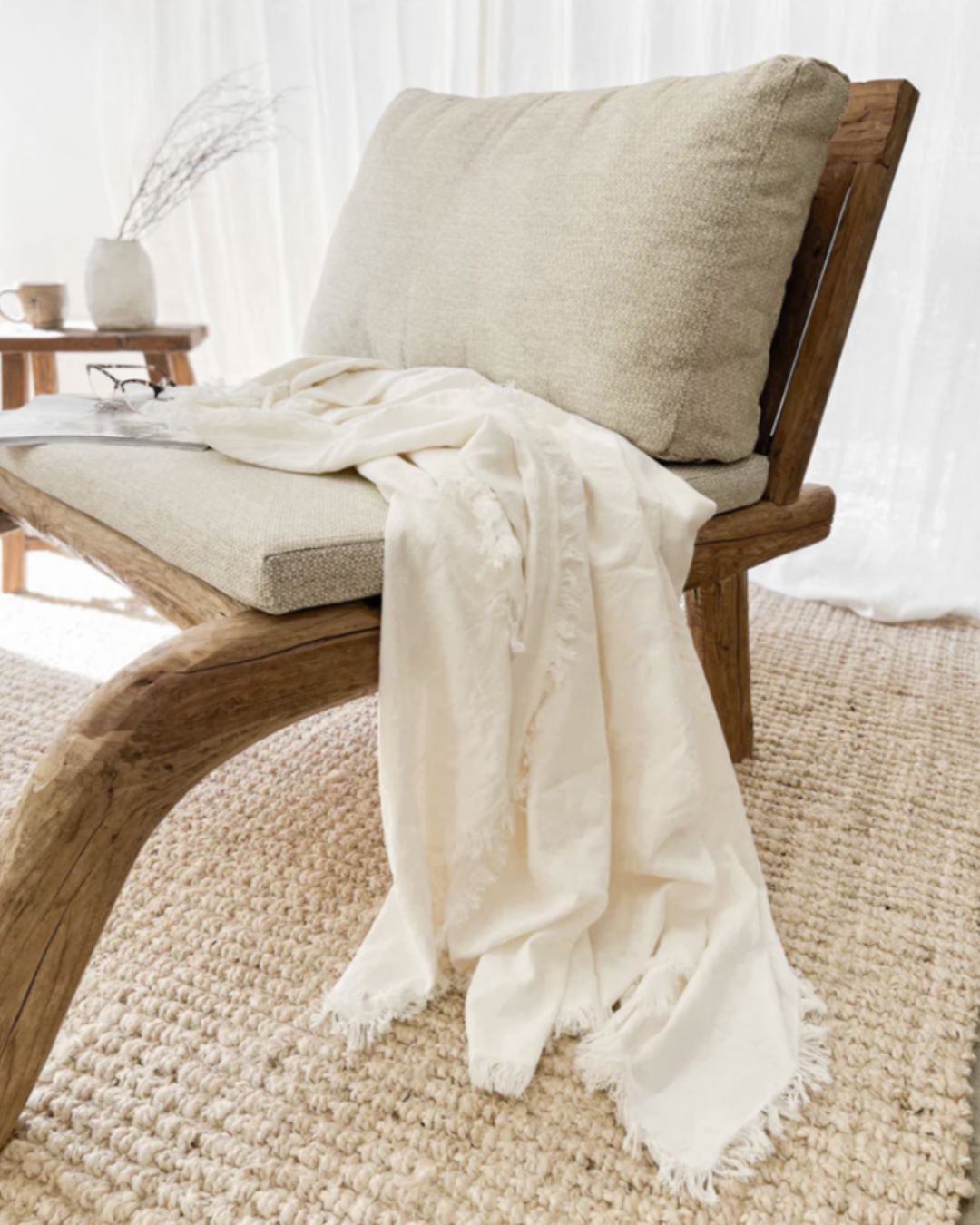 Wooden chair with a beige cushion and white blanket on a textured rug