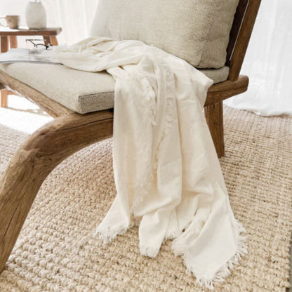 Wooden chair with a beige cushion and white blanket on a textured rug