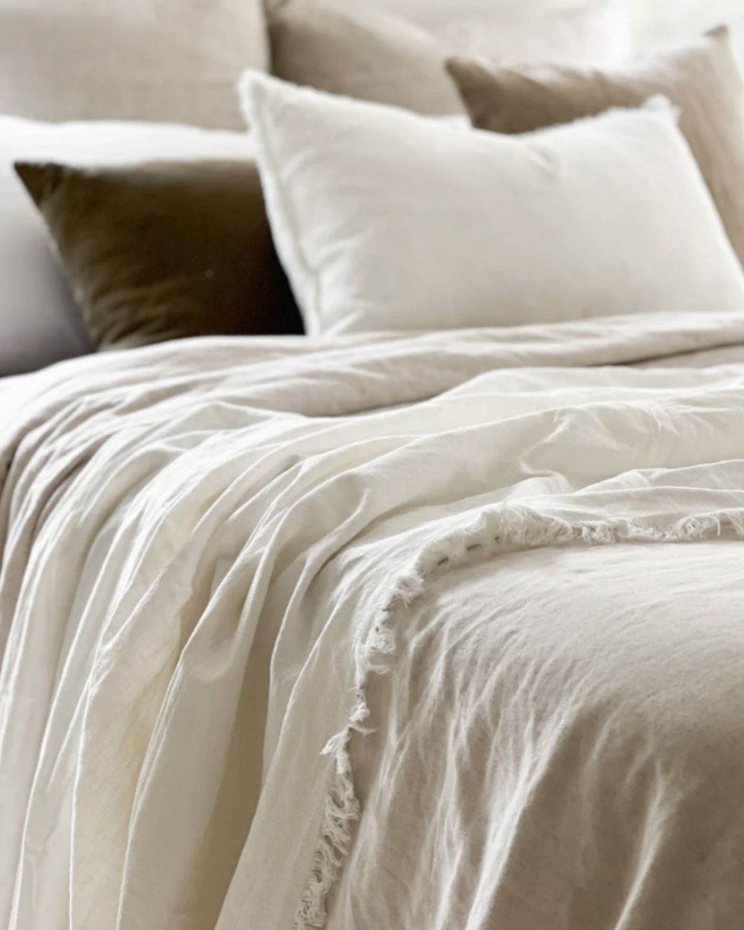 Neatly made bed with beige bedding and pillows in a softly lit room.