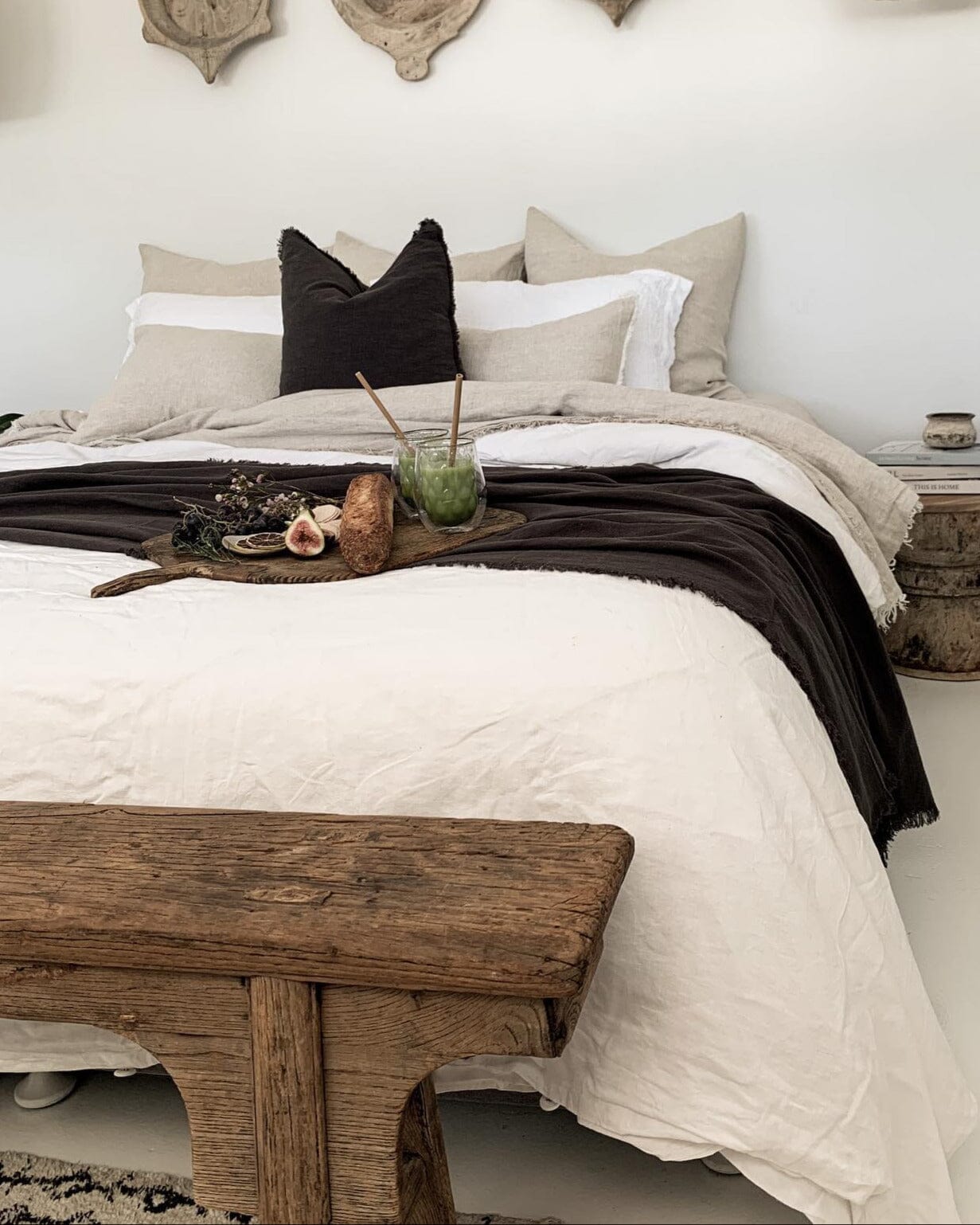 Neatly made bed with neutral bedding and a wooden bench in a bedroom setting.