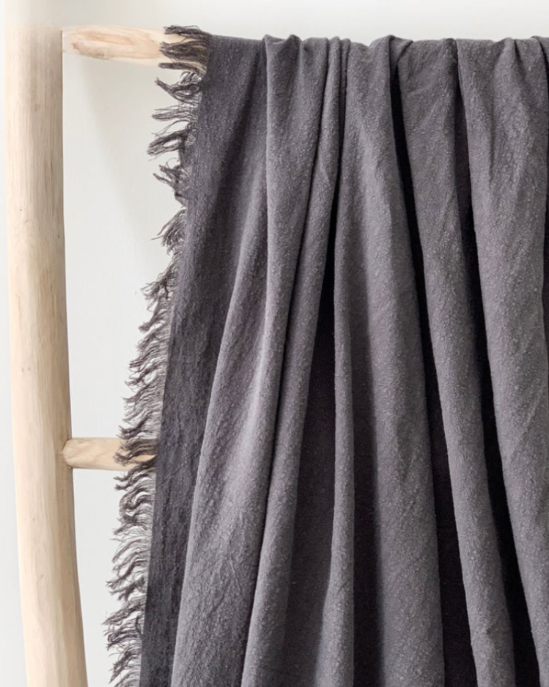 Gray throw blanket draped over a wooden ladder against a white wall