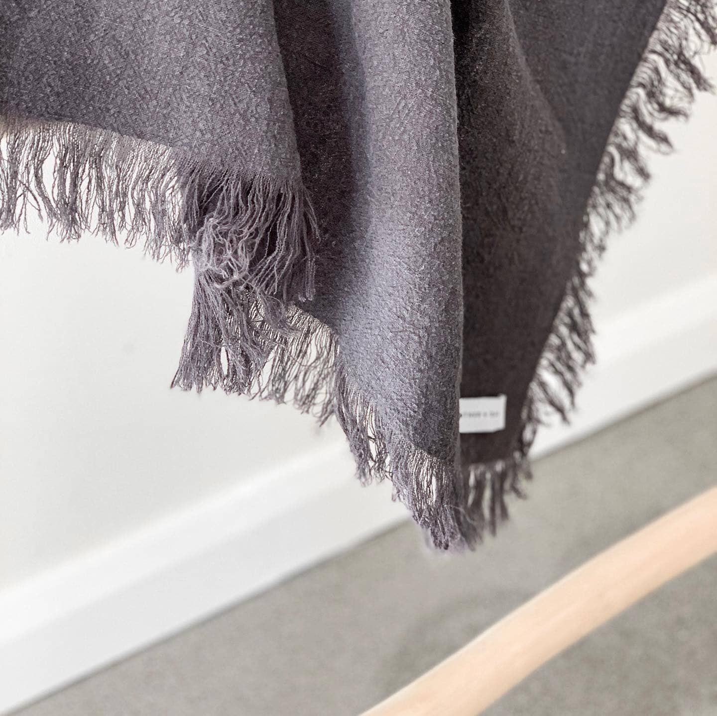 Gray fringed blanket draped over a white surface with a neutral background