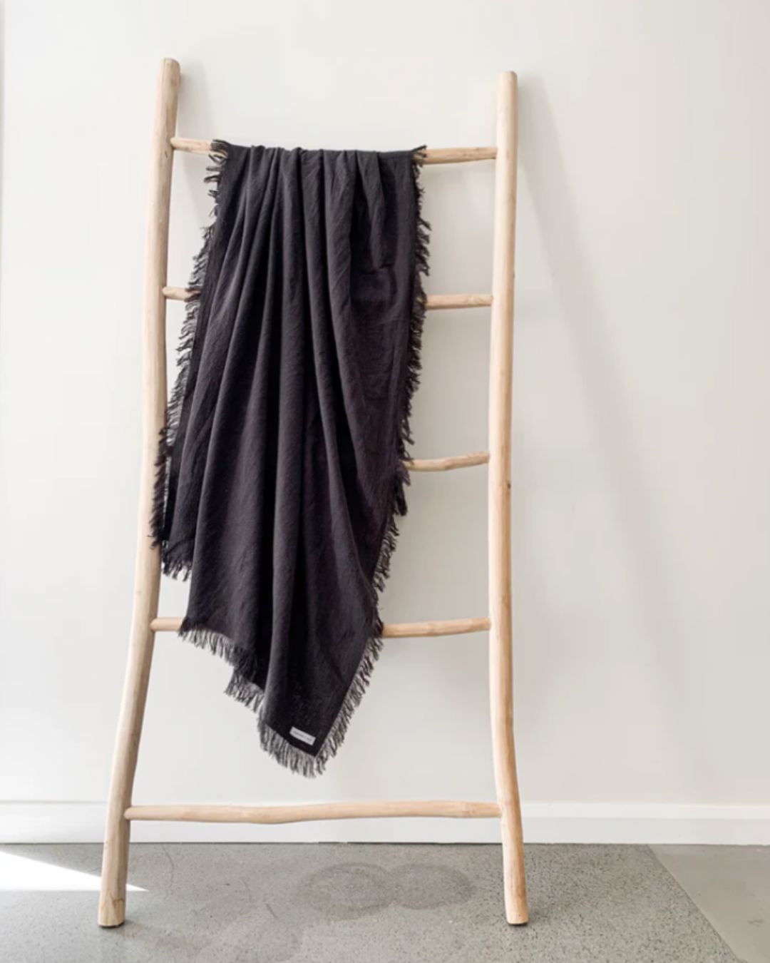 Black blanket draped over a wooden ladder against a white wall