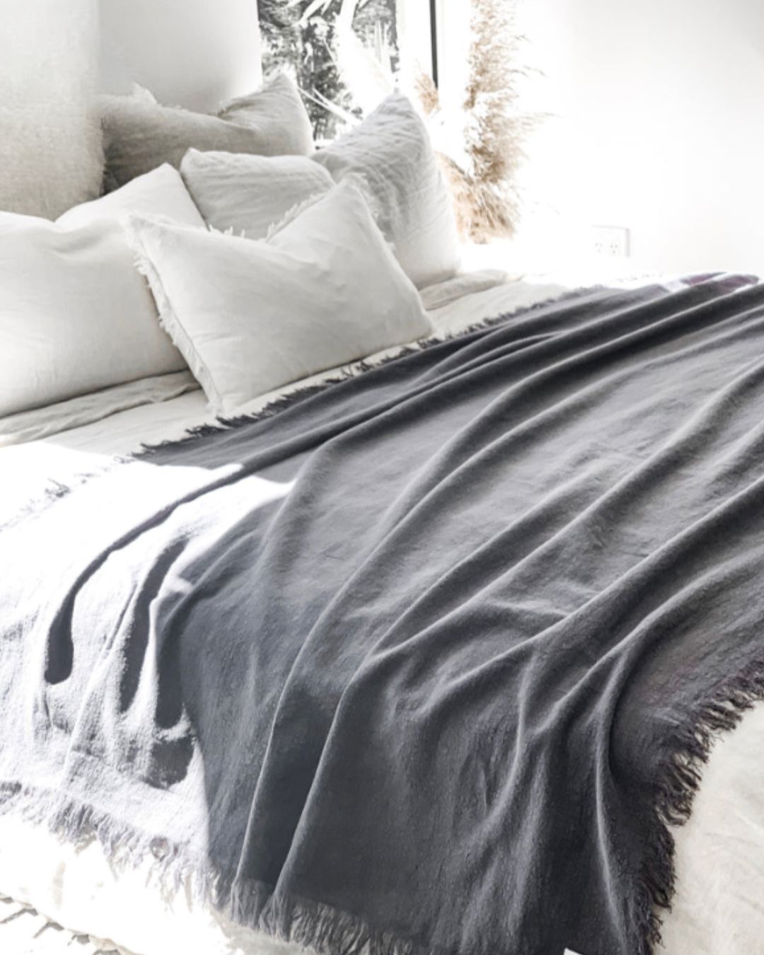 Gray blanket draped over a bed with white pillows in a softly lit room.