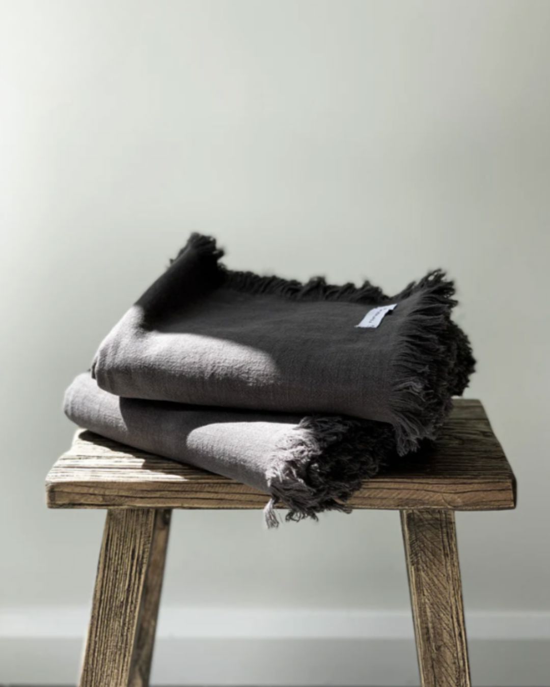 Folded dark gray blanket on a wooden stool against a light background