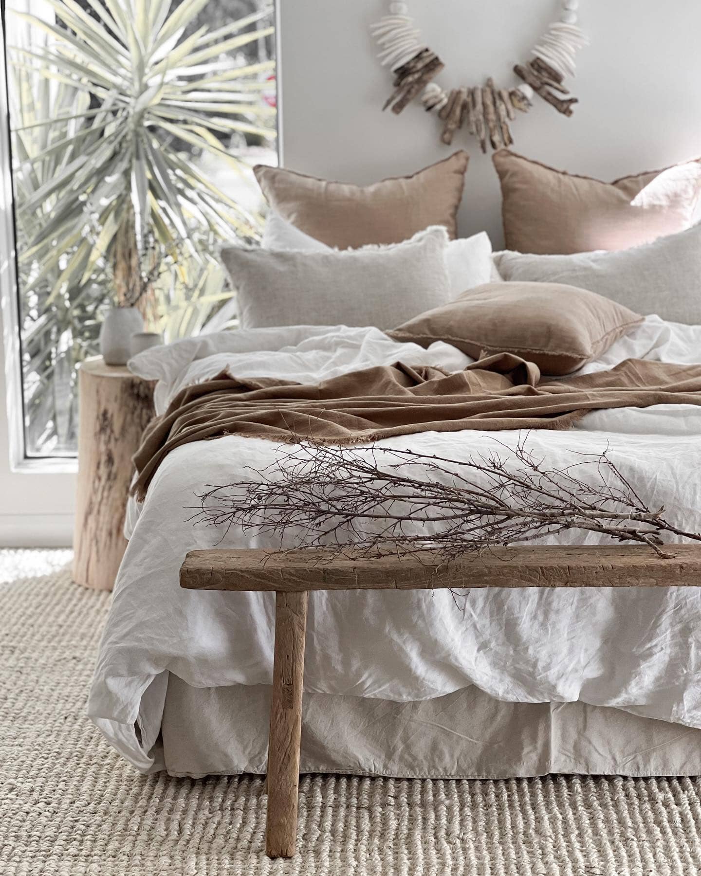 Neatly made bed with beige and white bedding in a bright bedroom.
