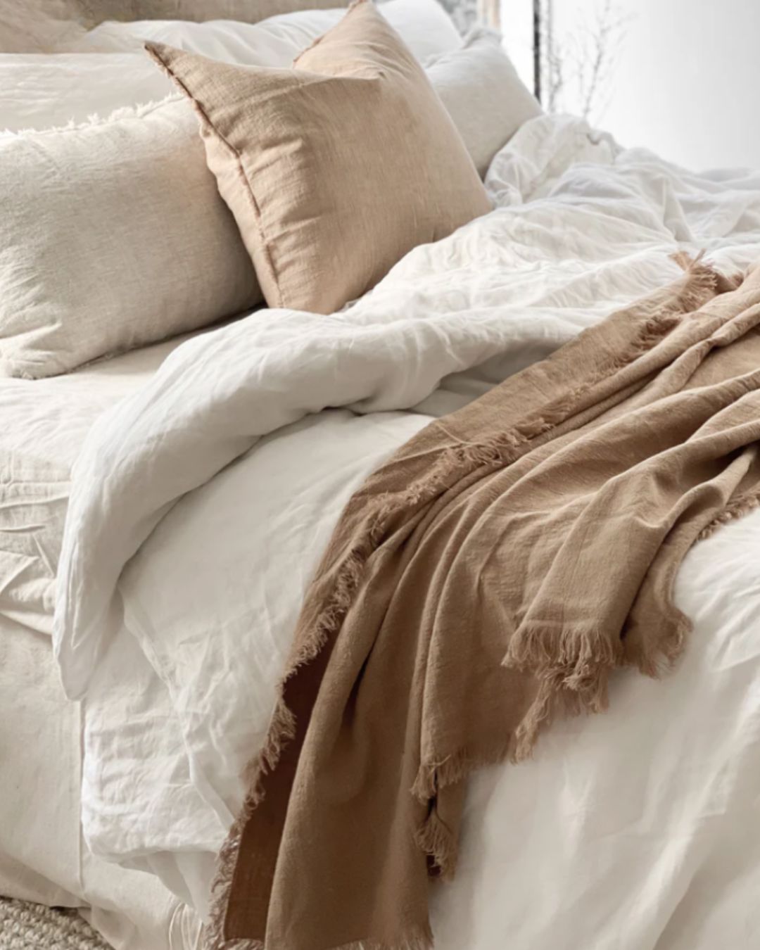 Neatly made bed with white bedding and brown throw blanket and pillow