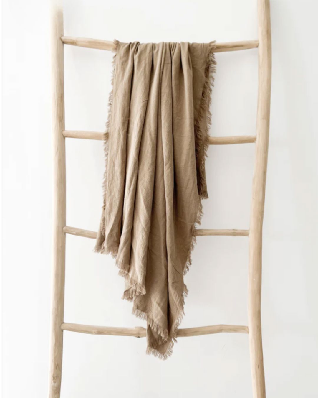 Beige blanket draped over a wooden ladder against a white background