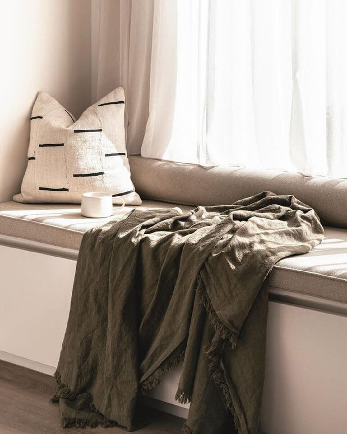 Cozy window seat with pillows and a blanket in a softly lit room.