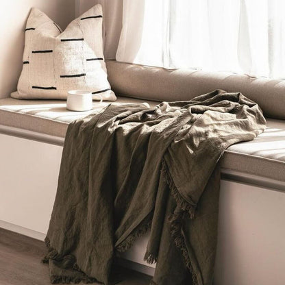 Cozy window seat with pillows and a blanket in a softly lit room.