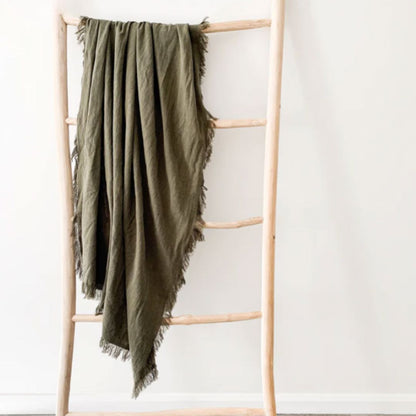 Green blanket draped over a wooden ladder against a white wall