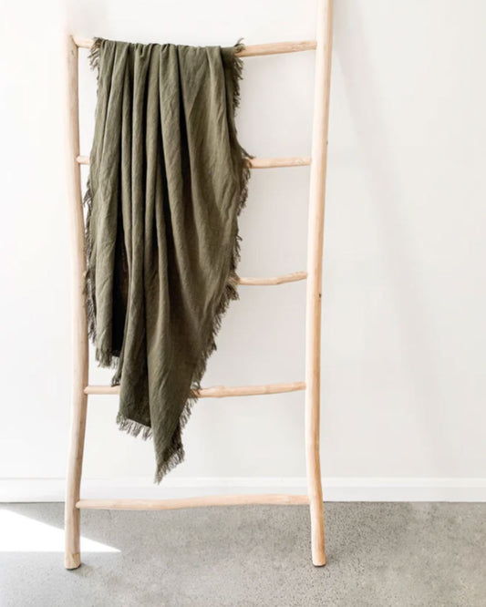 Green blanket draped over a wooden ladder against a white wall