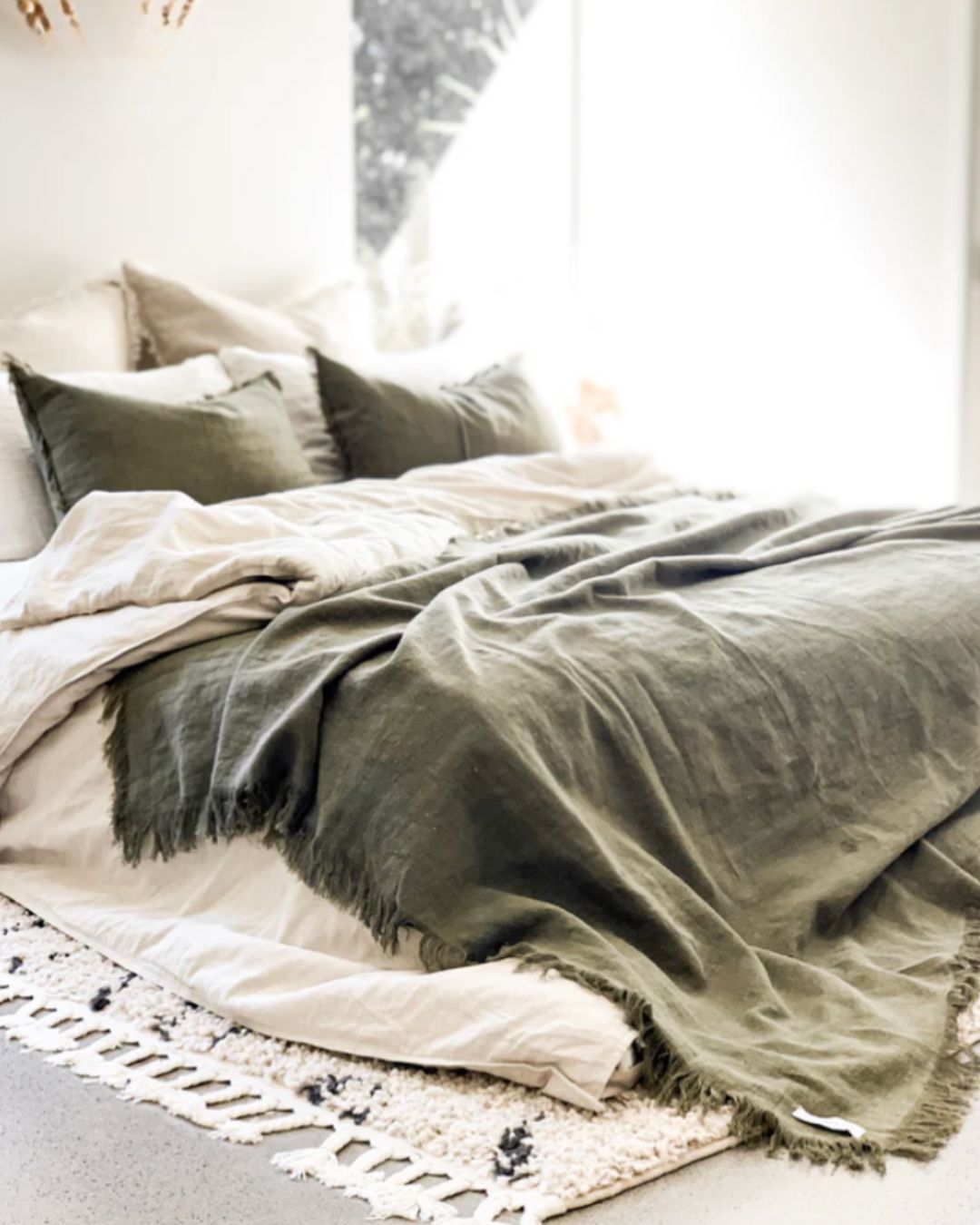 Neatly made bed with green blanket and pillows in a softly lit room.