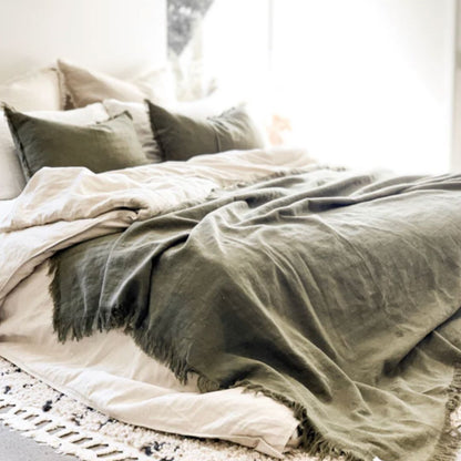 Neatly made bed with green blanket and pillows in a softly lit room.