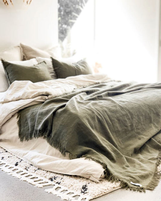 Neatly made bed with green blanket and pillows in a softly lit room.