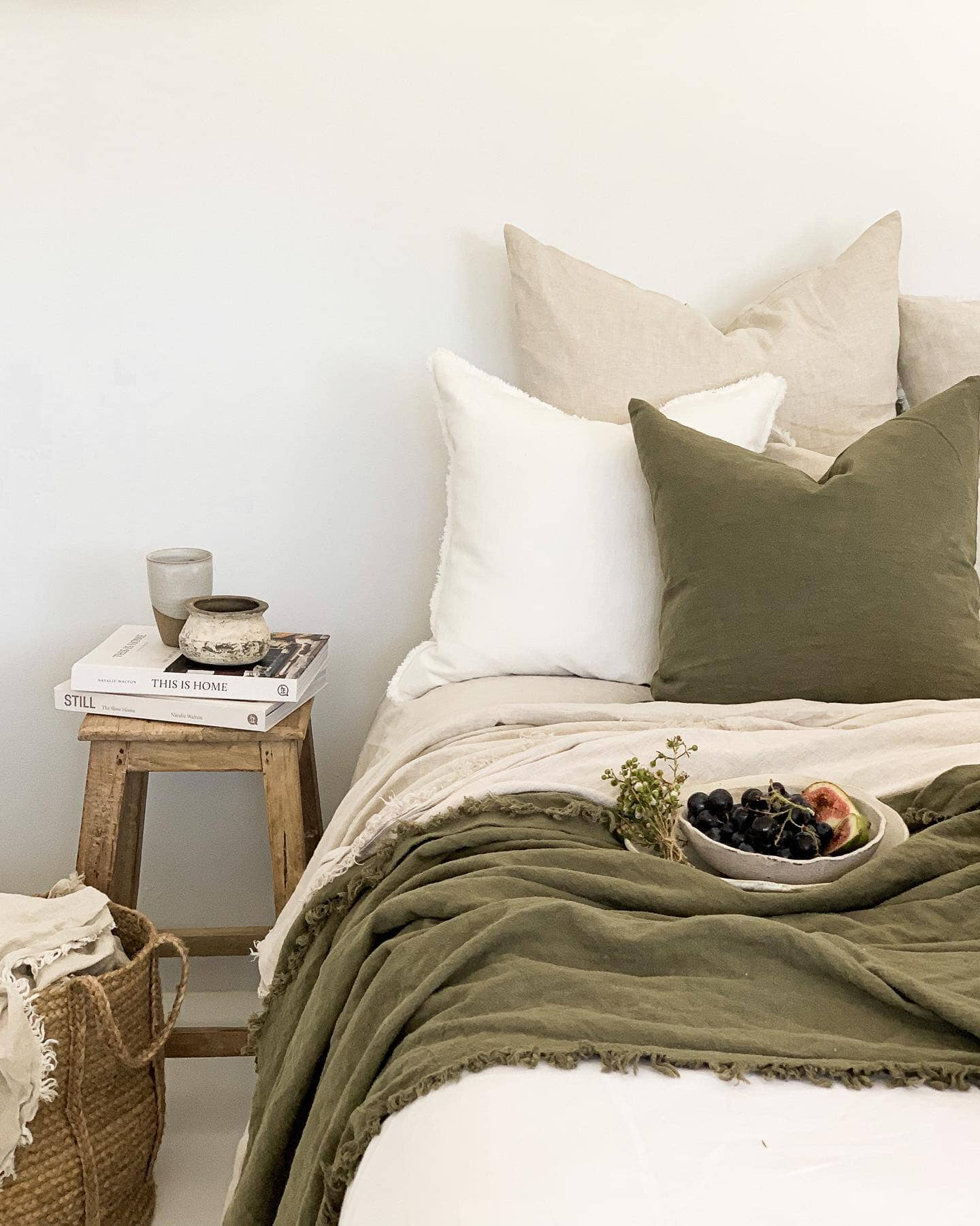 Bedroom with a bed featuring green and white bedding, a wooden side table with books and a candle, and a woven basket.