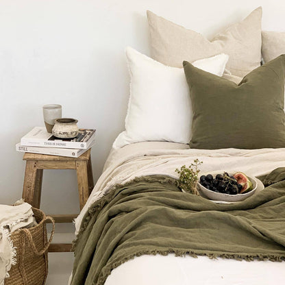 Bedroom with a bed featuring green and white bedding, a wooden side table with books and a candle, and a woven basket.
