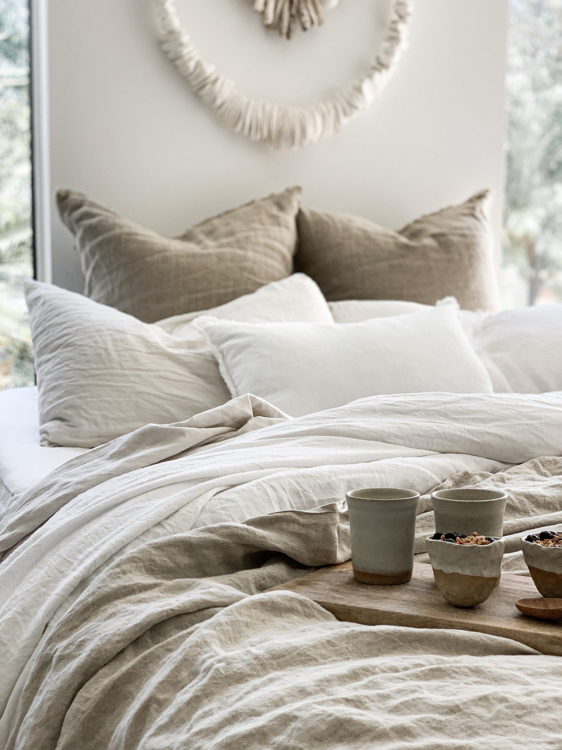 Neatly made bed with beige and white bedding, pillows, and a small wooden table with decorative items.