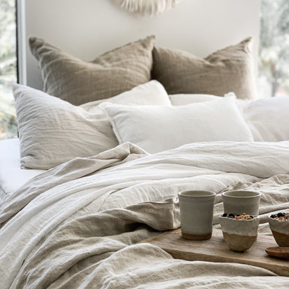 Neatly made bed with beige and white bedding, pillows, and a small wooden table with decorative items.