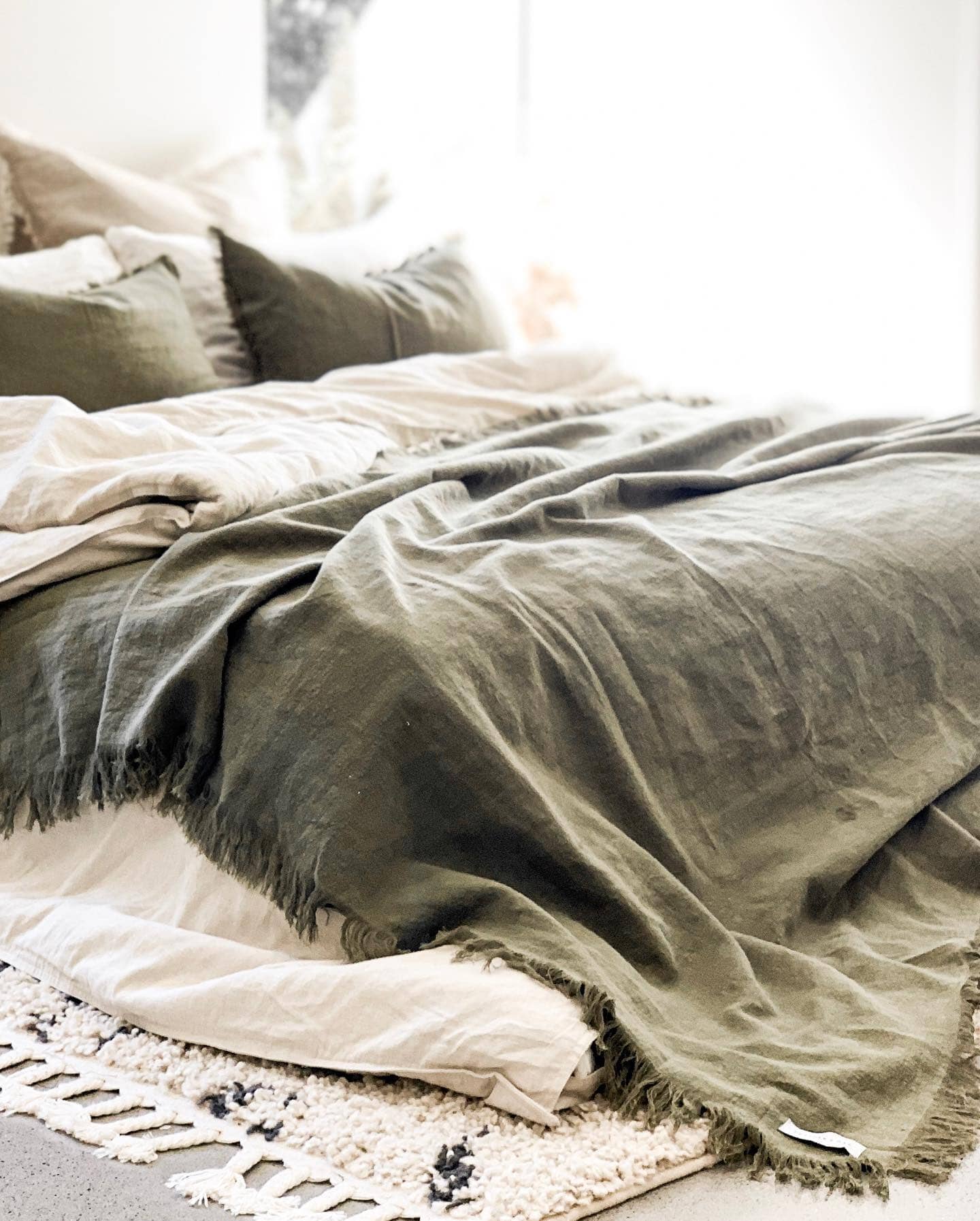 Green textured blanket draped over a bed with pillows in a softly lit room.