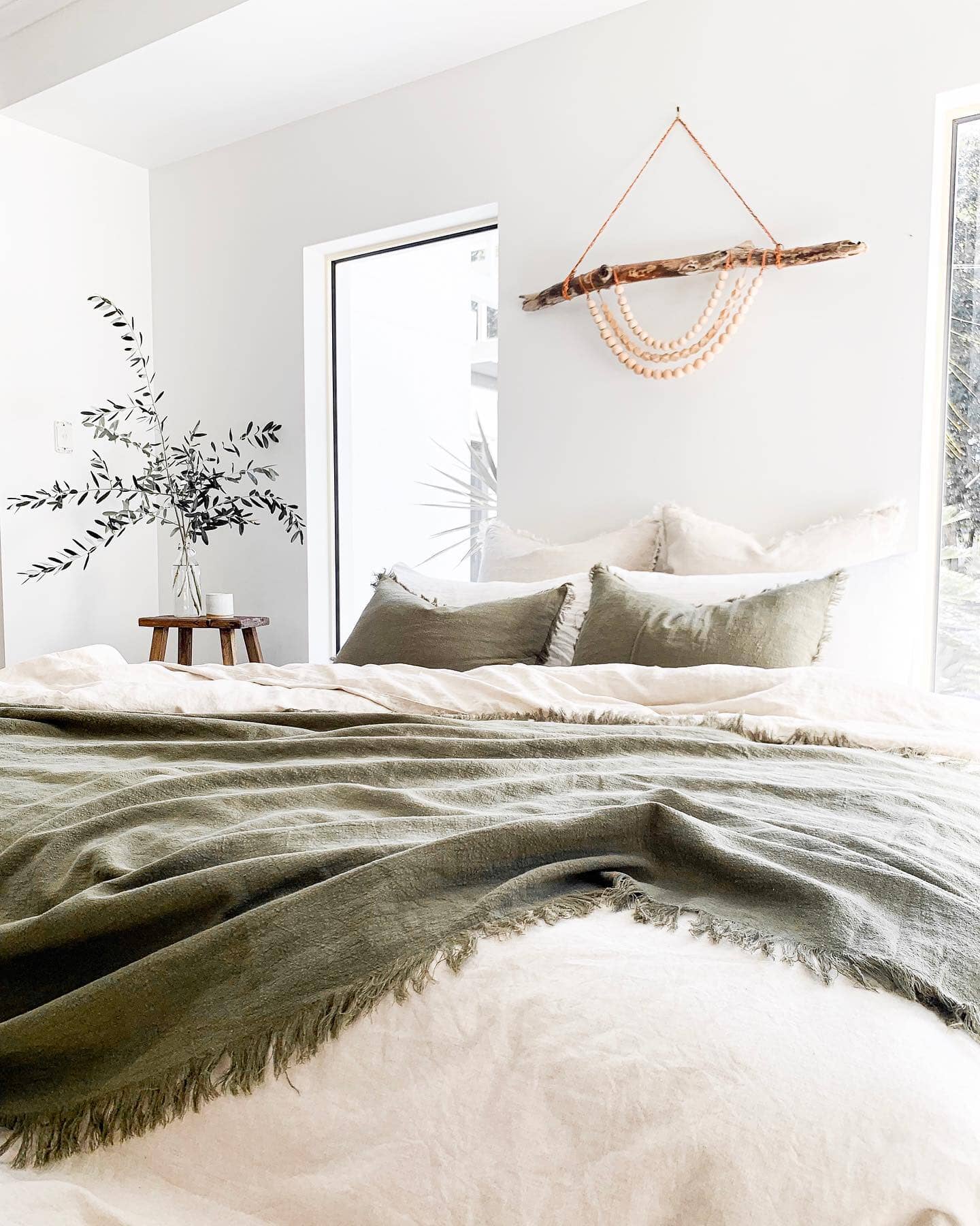 Neatly made bed with green blanket and pillows in a bright bedroom.