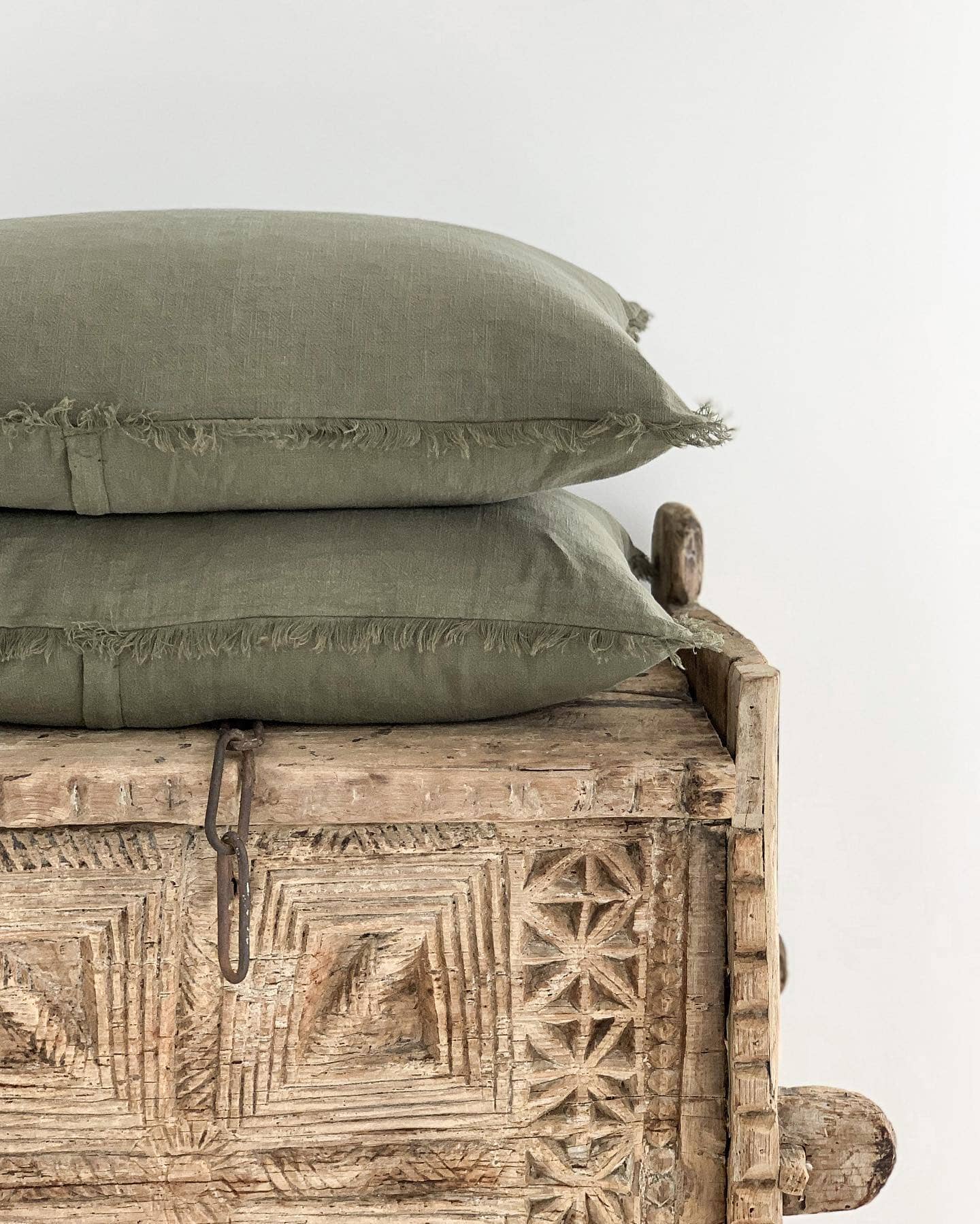 Two green pillows stacked on a wooden bench with intricate carvings against a white background