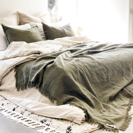 Neatly made bed with green and beige bedding in a softly lit room.