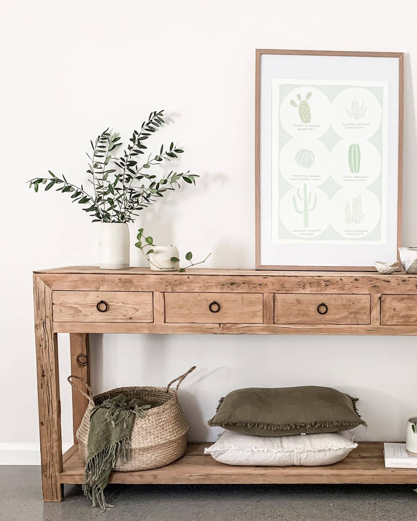 Wooden console table with decorative items including a plant, framed artwork, and pillows in a room.