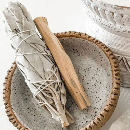 Ceramic bowl with sage and a wooden stick on a light background
