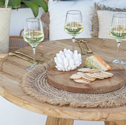 Wooden table with cheese, crackers, and wine glasses on a patio setting