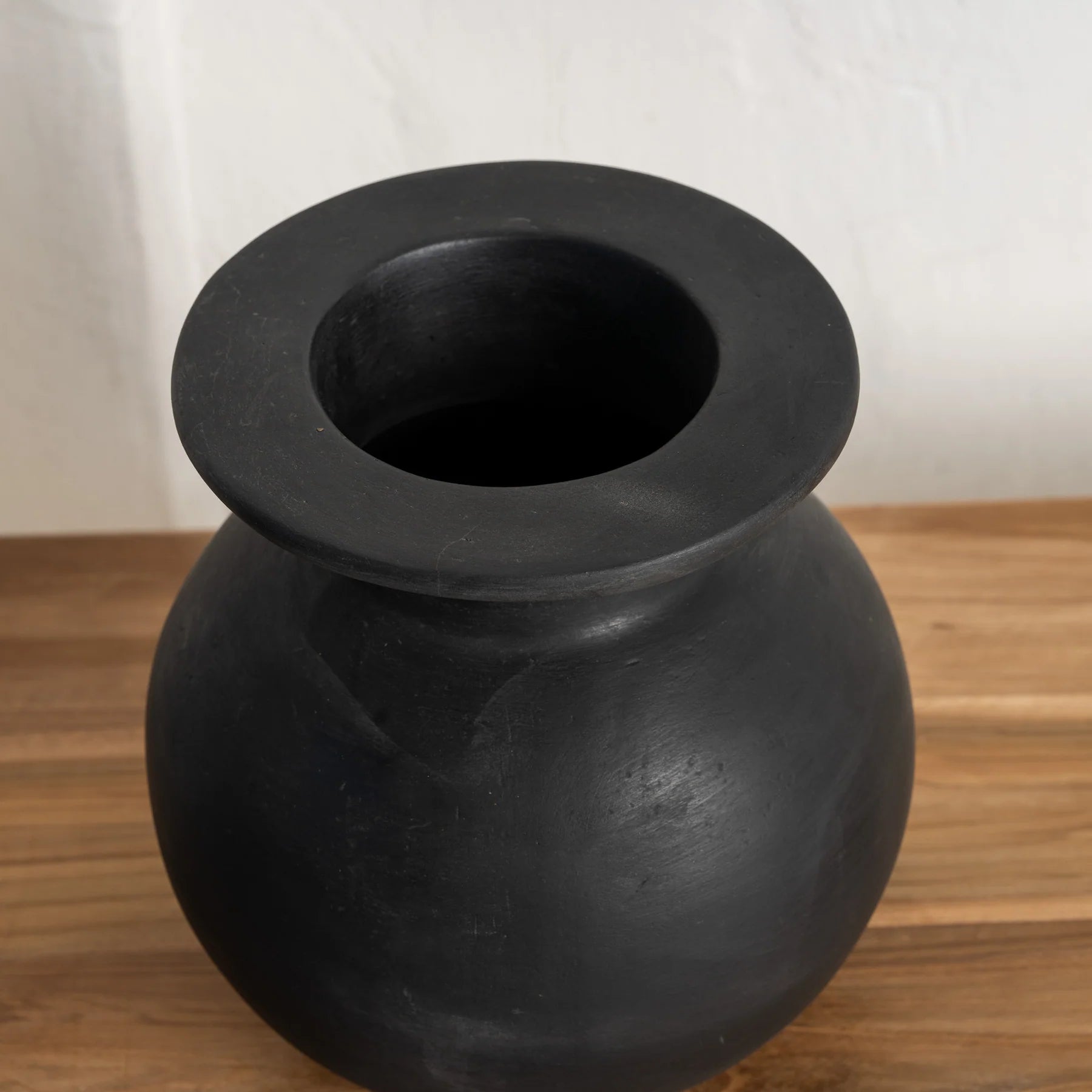Black ceramic vase on a wooden surface with a white background by Sun Republic