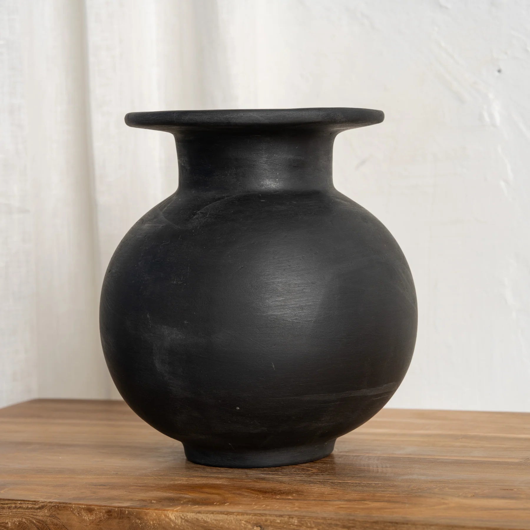 Black ceramic vase on a wooden surface with a white background by Sun Republic