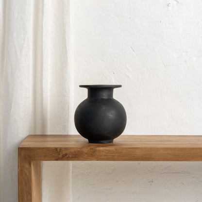 Black vase on a wooden table with a white curtain in the background