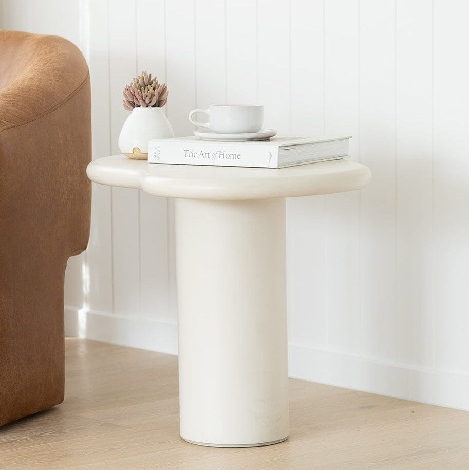 Small round side table with a book, cup, and plant in a minimalistic room.
