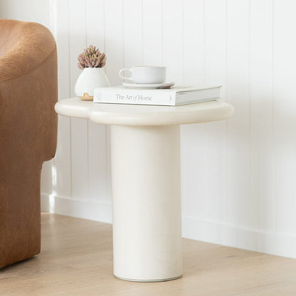 Small round side table with a book, cup, and plant in a minimalistic room.