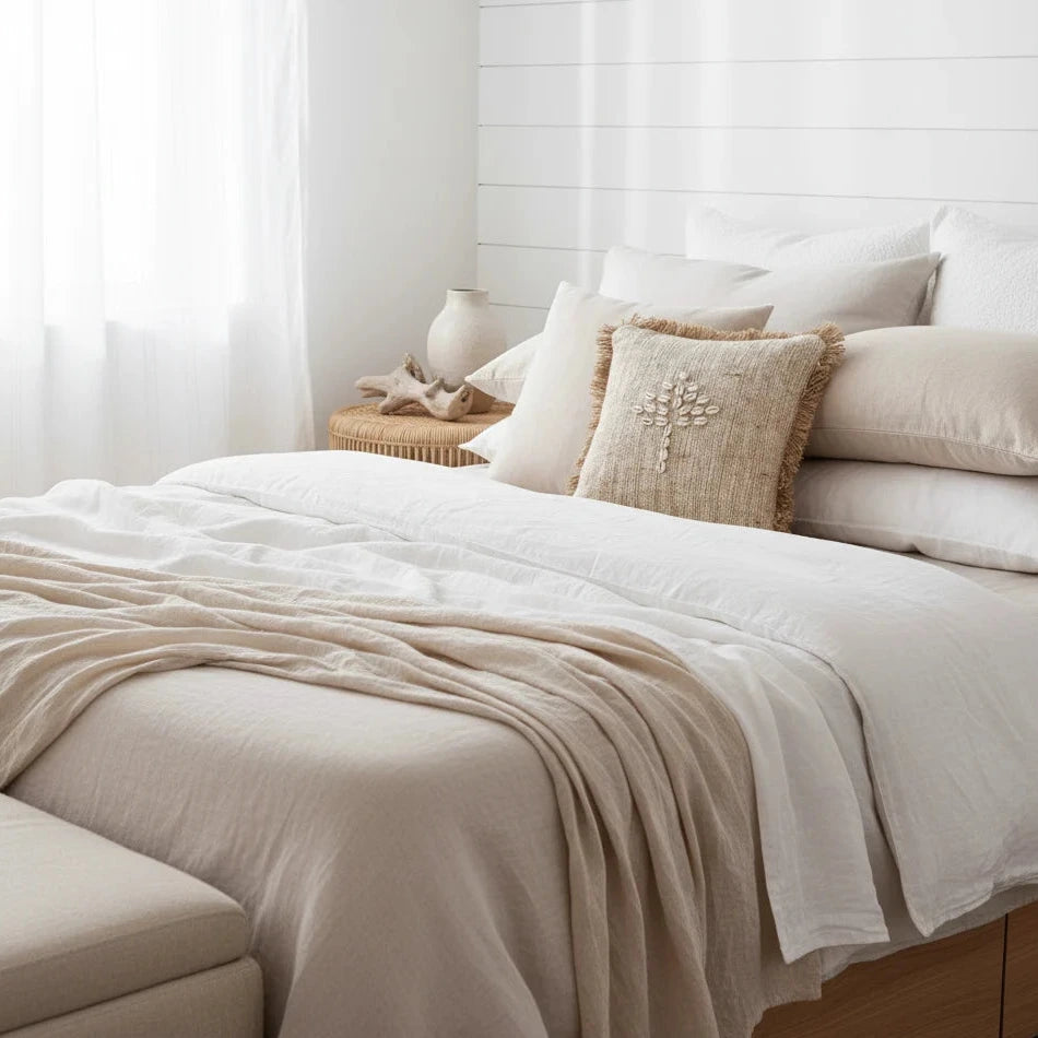 Neatly made bed with beige and white bedding in a bright bedroom.