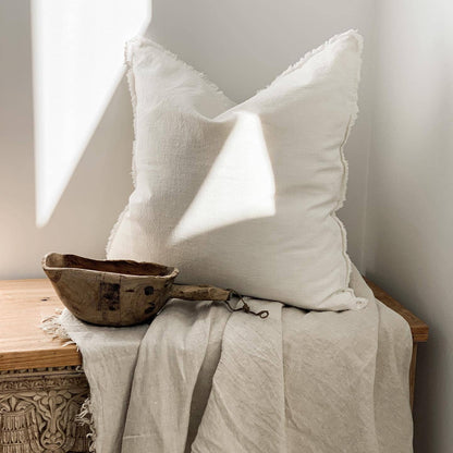 White pillow and wooden bowl on a textured surface with soft lighting
