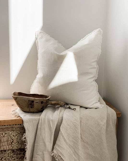 White pillow and wooden bowl on a textured surface with soft lighting