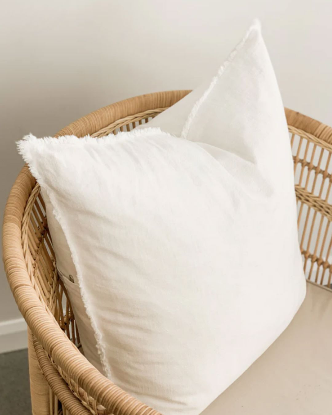 White pillows on a wicker chair against a neutral wall