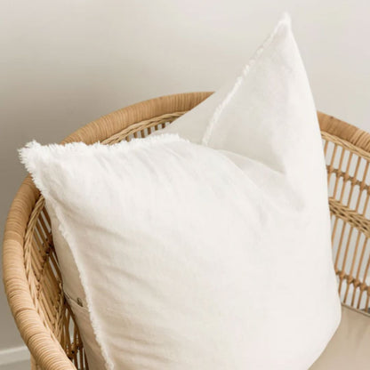 White pillows on a wicker chair against a neutral wall
