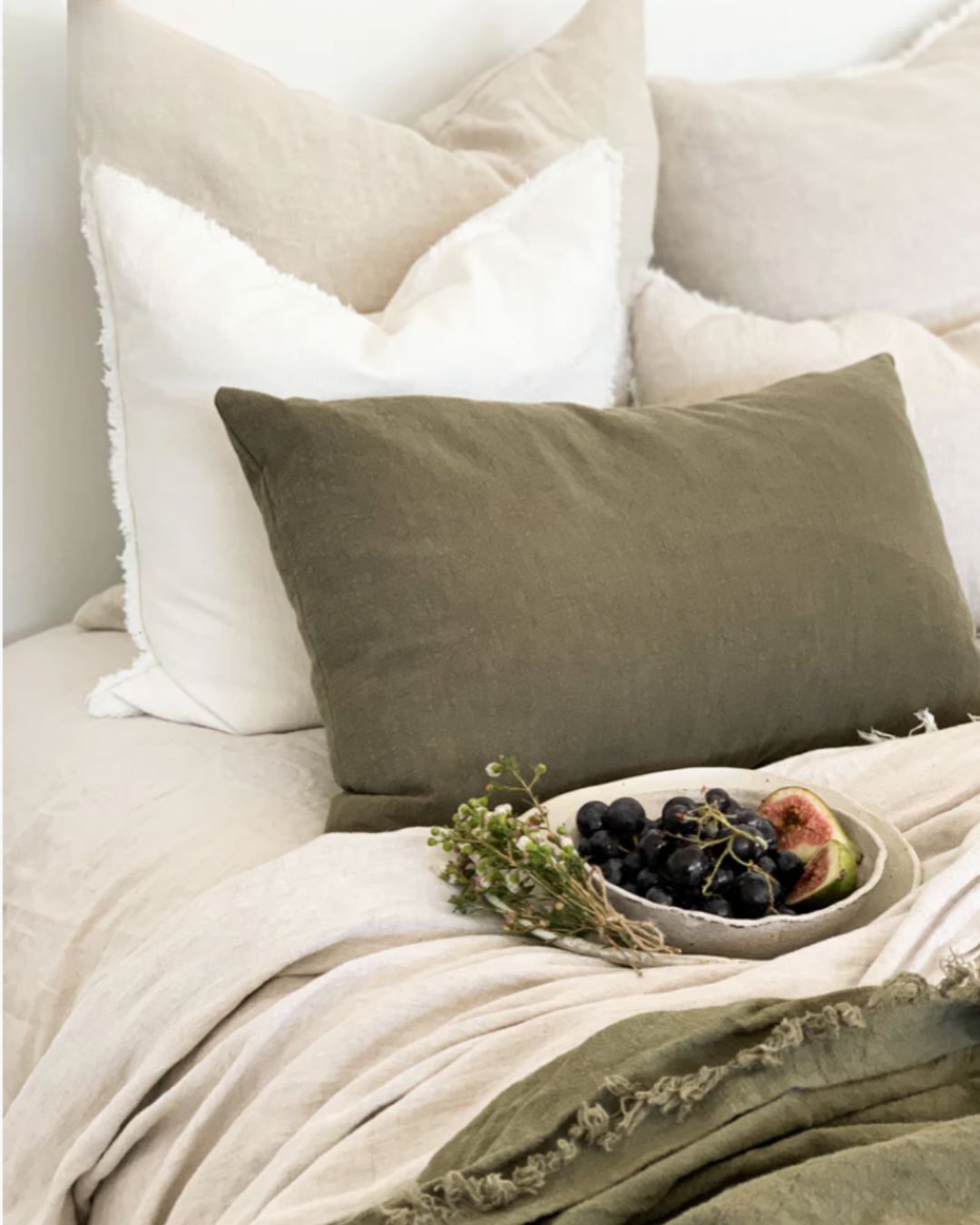Cozy bedroom scene with pillows and a bowl of fruit on a bed.