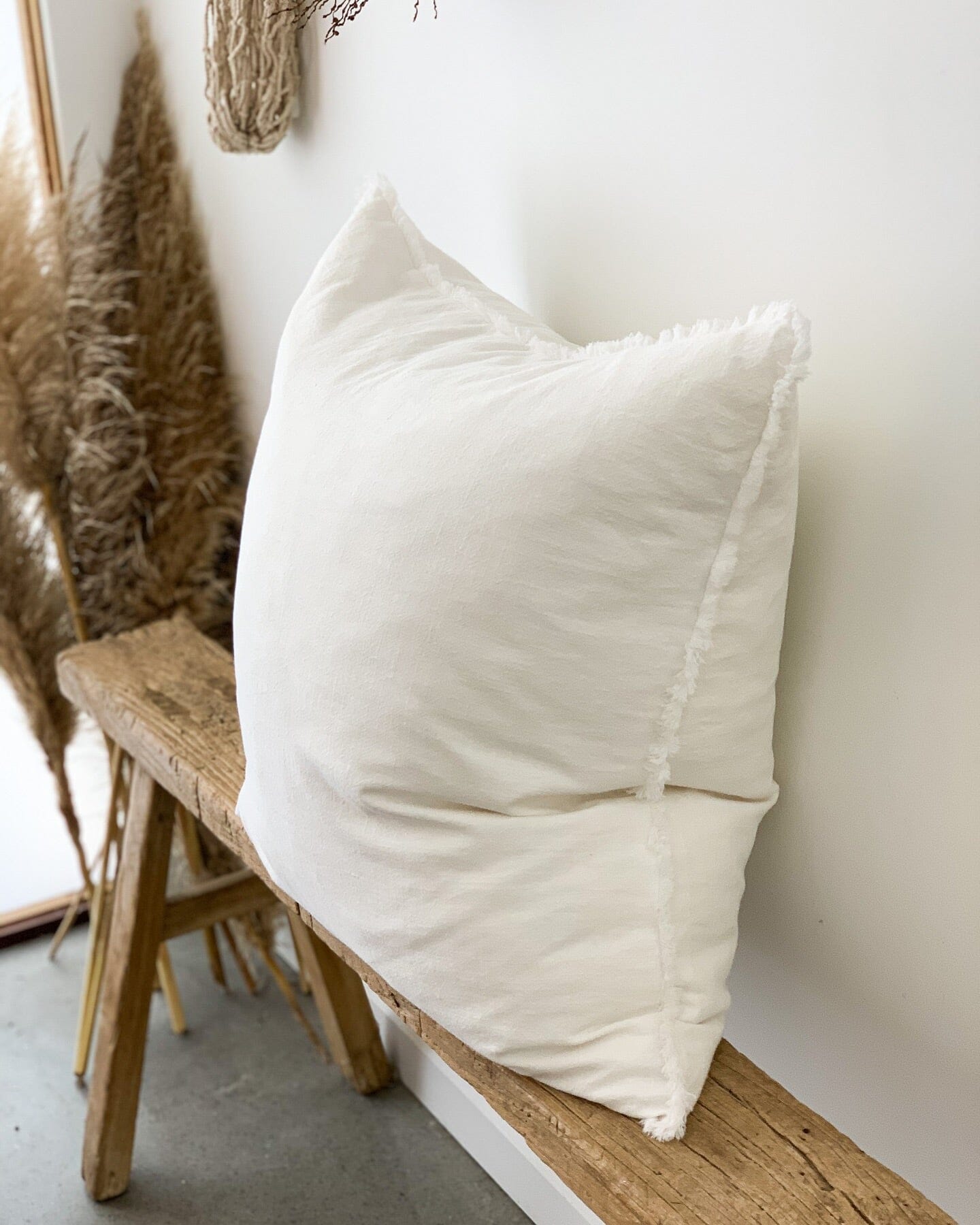 White pillow on a wooden stool against a white wall