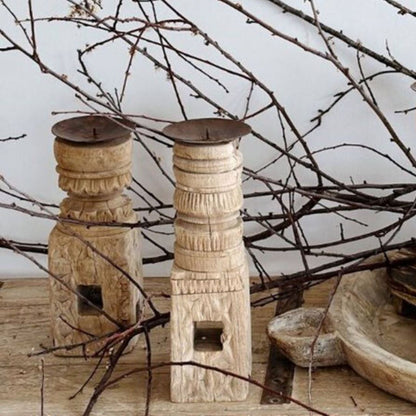 Two wooden candle holders with intricate designs on a surface with branches in the background.