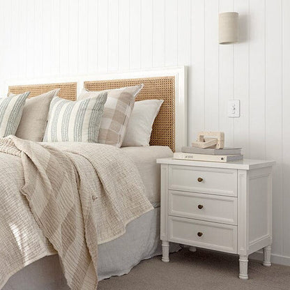 Neatly made bed with striped pillows and a white nightstand in a bedroom.