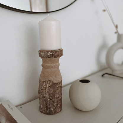 A rustic vintage Indian Gindi wooden candle holder placed on a table, with a white candle on top and a round mirror reflecting the candle holder.