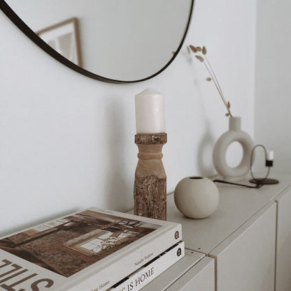 A Vintage Indian Gindi Wooden Candle Tower placed on a shelf with a mirror above it, a candle on top, a book, and a decorative ball to the right.