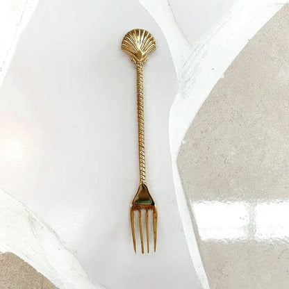Gold shell-handled fork on a white plate with a beige napkin.